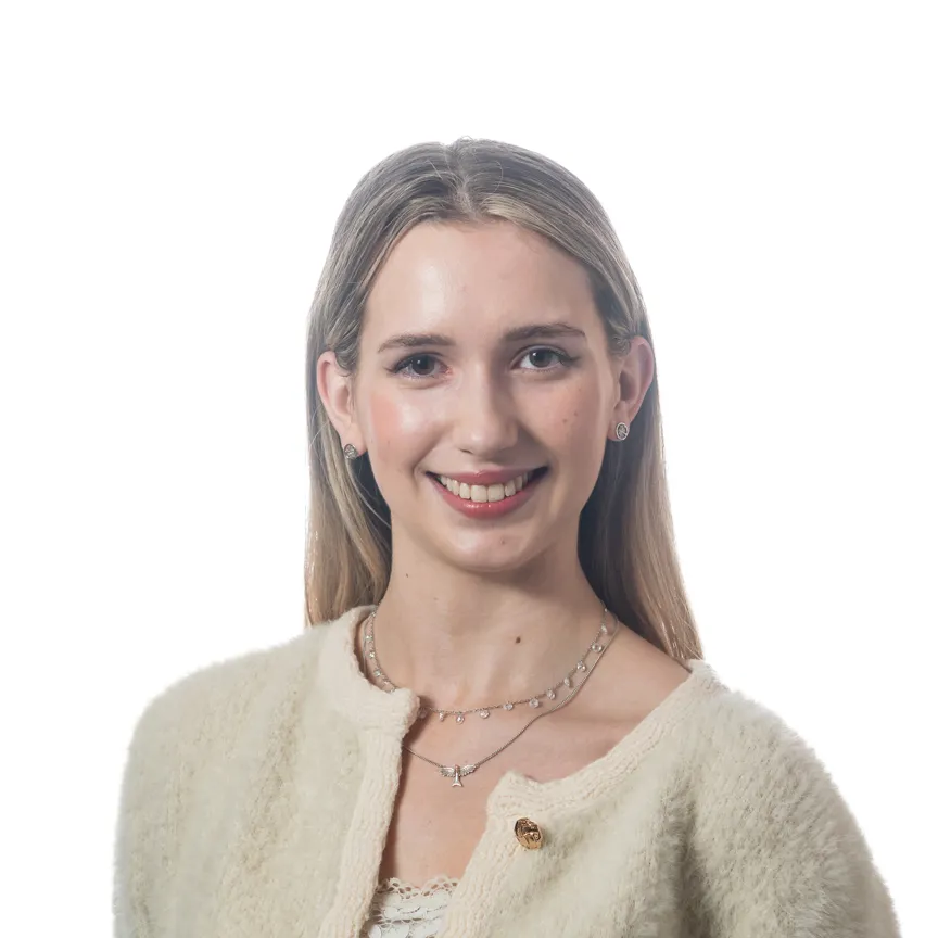 Smiling young woman with long blonde hair wearing a cream-colored fuzzy cardigan and layered silver necklaces.
