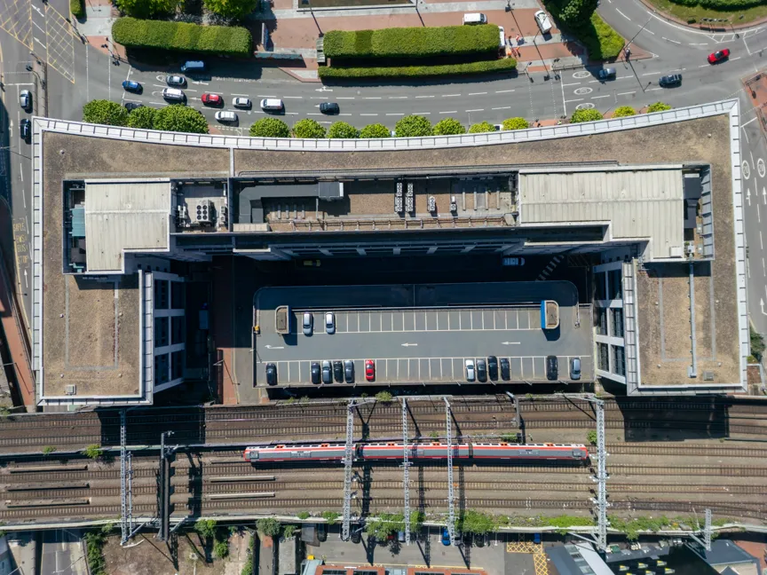 Aerial view of an urban building with a large parking lot on its roof, train tracks and a train below, and roads with cars above.