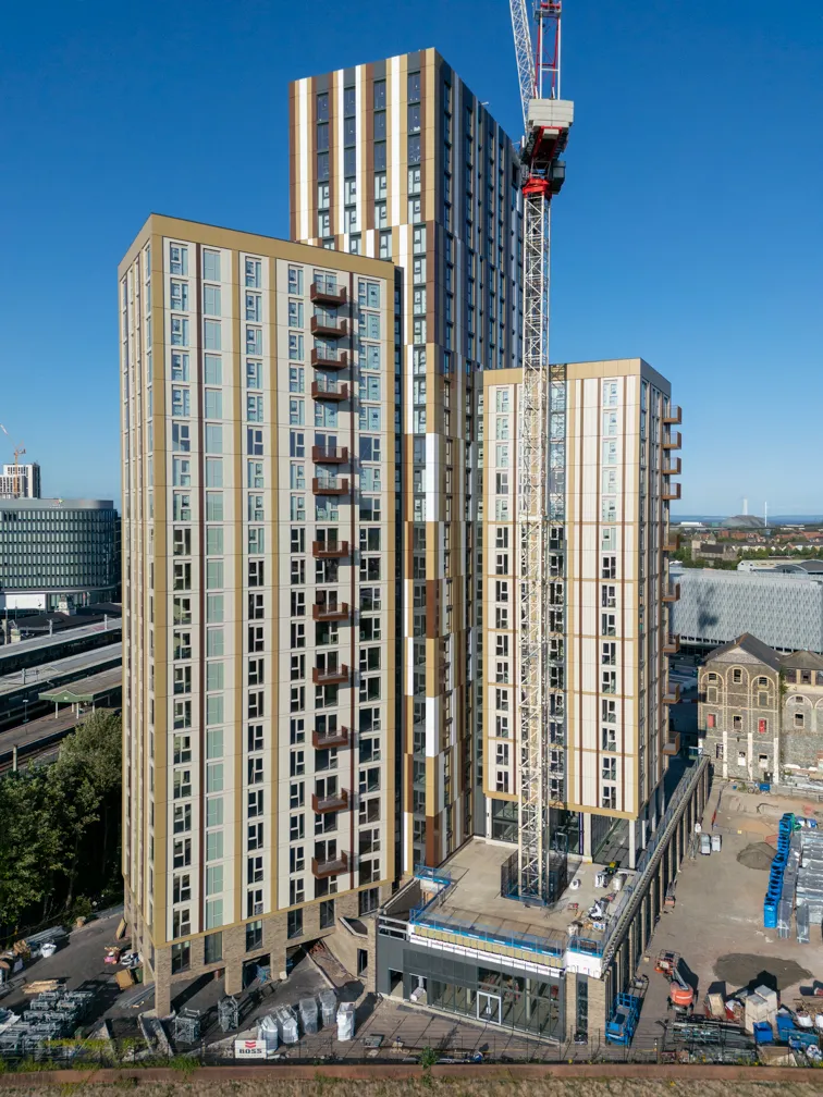 Tall modern residential buildings under construction with a central crane and clear blue sky.