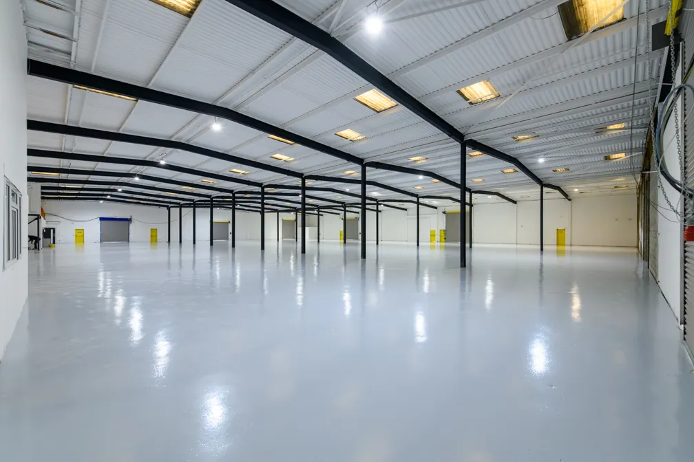 Spacious empty warehouse interior with polished floor, white walls, black ceiling beams, and yellow doors.