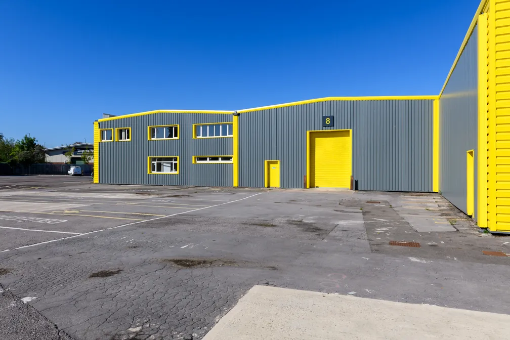 Industrial warehouse building with gray walls and yellow trim around doors and windows under a clear blue sky.