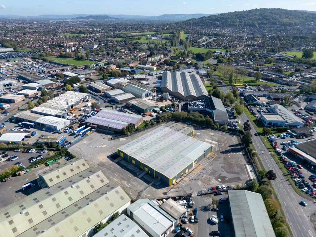 Aerial view of an industrial area with warehouses, parking lots, roads, and residential neighborhoods in the distance under a clear sky.