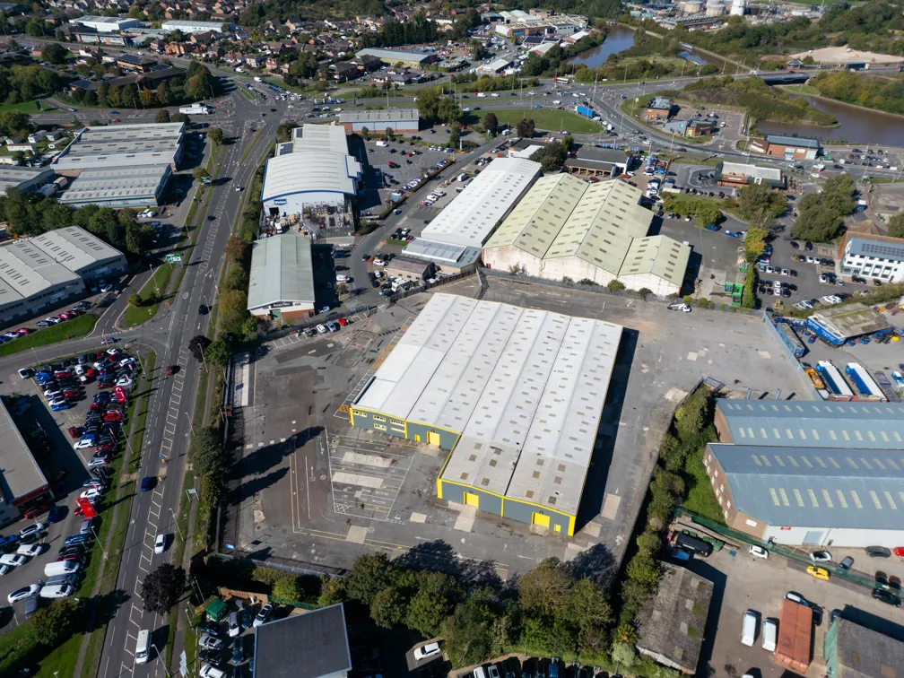 Aerial view of an industrial area with multiple warehouses, parking lots, roads, and surrounding greenery under daylight.