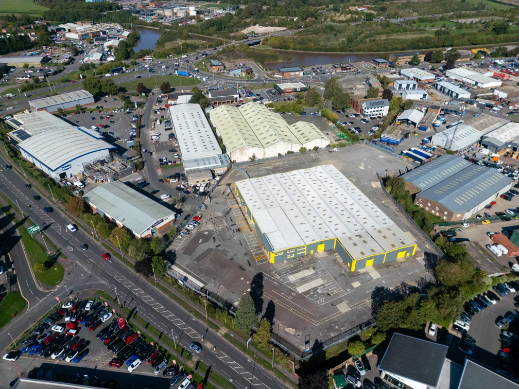 Aerial view of an industrial area with multiple warehouses, parking lots, and surrounding roads with vehicles.