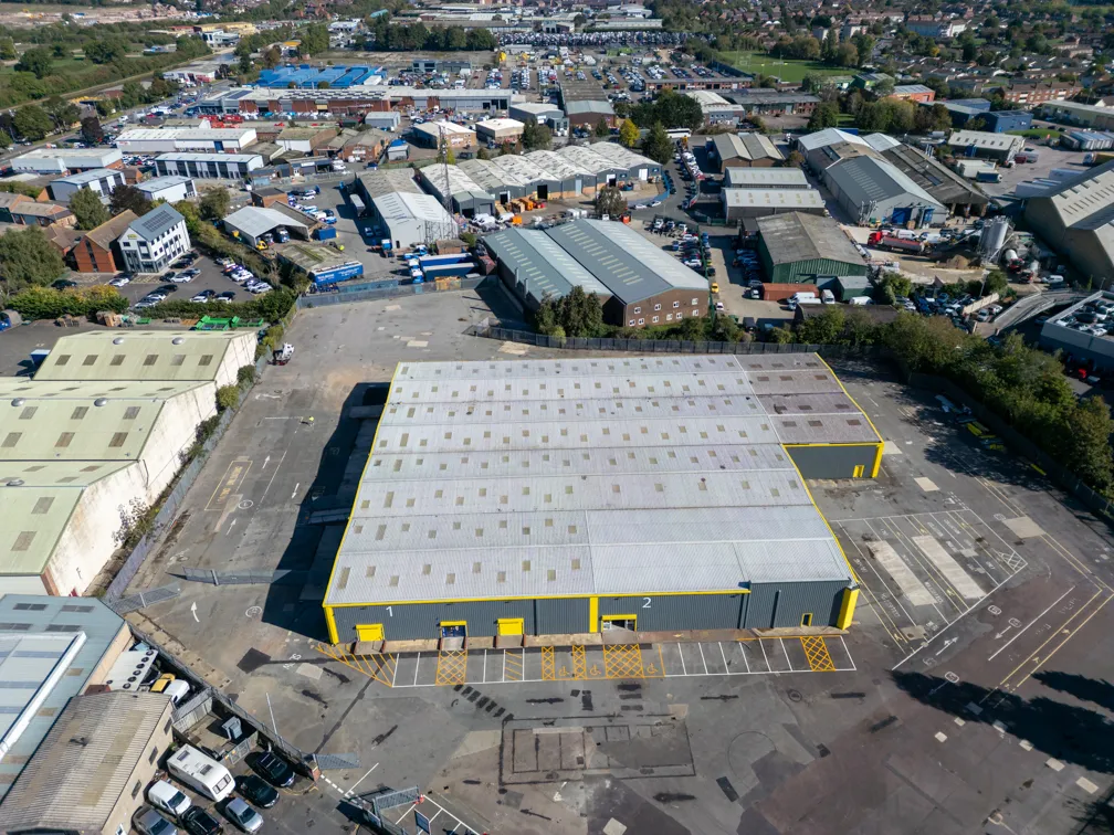Aerial view of a large industrial warehouse with yellow accents in a busy industrial park surrounded by multiple smaller buildings and parking areas.