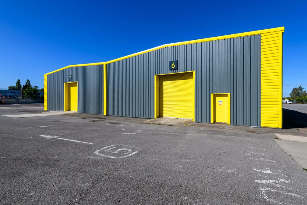 Gray industrial warehouse with bright yellow trim and doors numbered 6 and 7 under a clear blue sky.