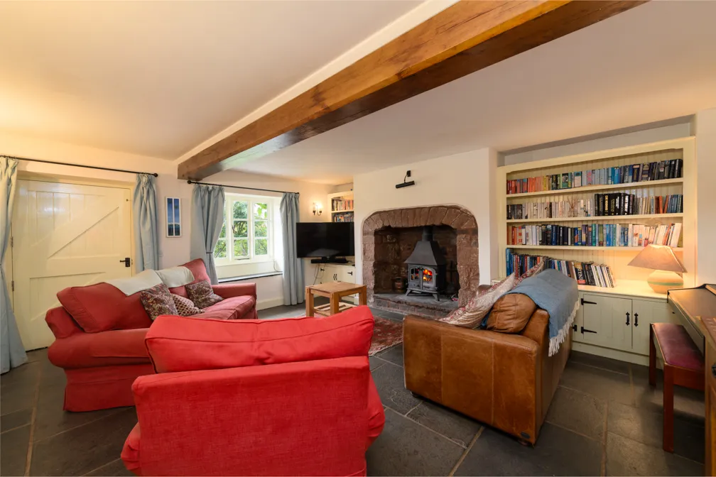 Cozy living room with red fabric sofas, a brown leather armchair, a wood-burning stove in a stone fireplace, a bookshelf with books, and a TV near a window with blue curtains.