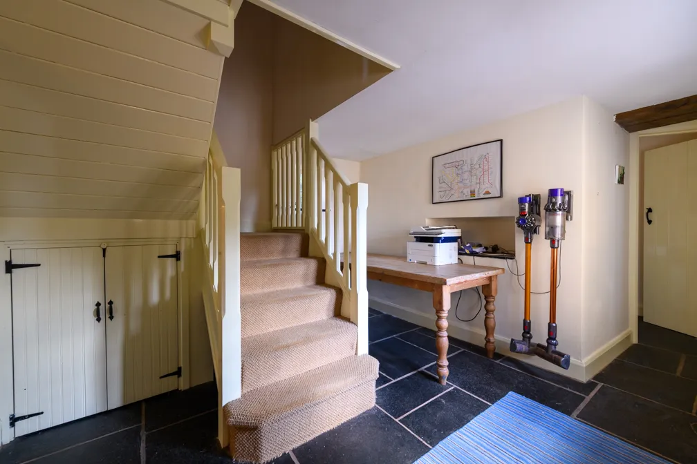 Cozy indoor space with carpeted stairs, a wooden table holding a printer, two upright vacuum cleaners mounted on the wall, and a map framed above the table.