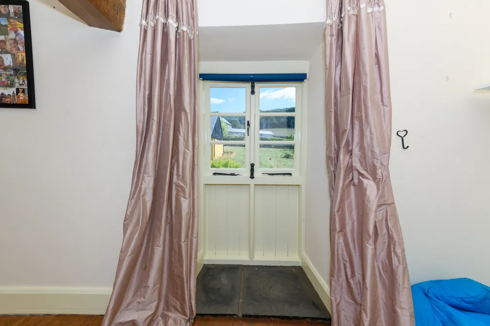 Small cream-colored interior door with window panes, flanked by pink curtains and looking out to a grassy yard with buildings and hills in the distance.
