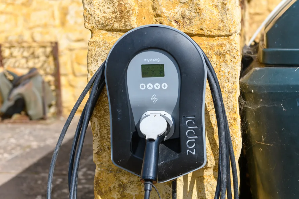 Zappi electric vehicle charging station mounted on a stone wall with a charging cable plugged in.