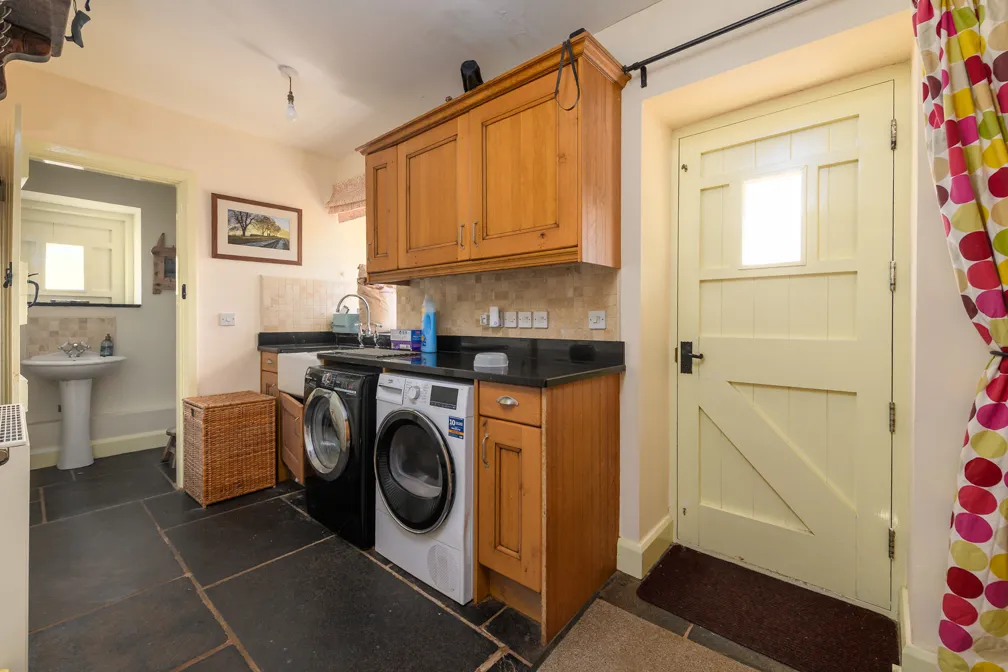 Laundry room with black and white front-loading washer and dryer under wooden cabinets, a sink, a door with window, and a glimpse of a bathroom with sink.