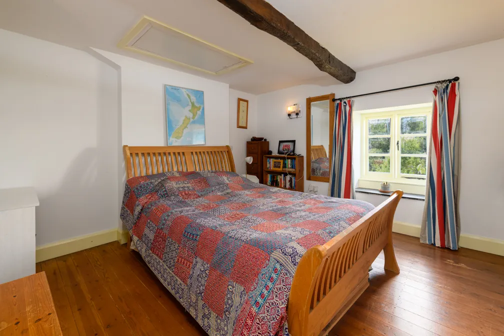 Bedroom with wooden bed covered by a patchwork quilt, wooden floor, window with striped curtains, and wall decorations.