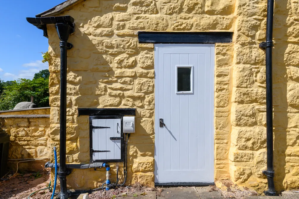 Yellow stone wall with a white door and a small white utility hatch, both framed with black trim, and black downspouts on each side.