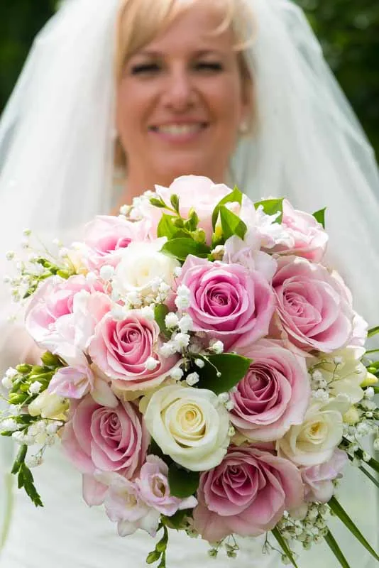 Bride holding a bouquet of pink and white roses with green leaves and baby's breath flowers.