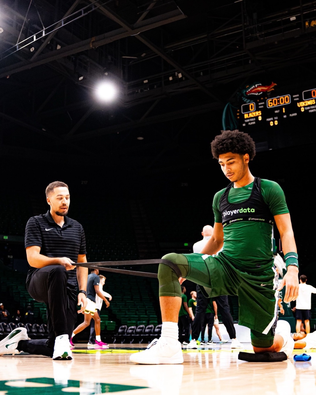 College basketball player warming up courtside with a coach