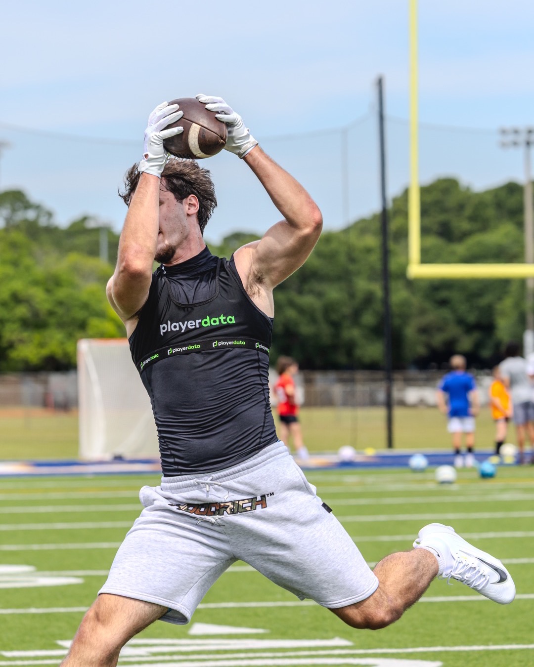 Player in a PlayerData vest leaping to catch a football at a high school practice