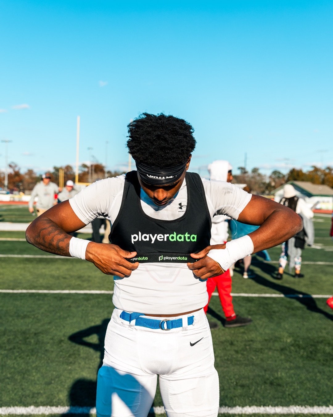 High school football player pulling on a black PlayerData GPS vest at practice