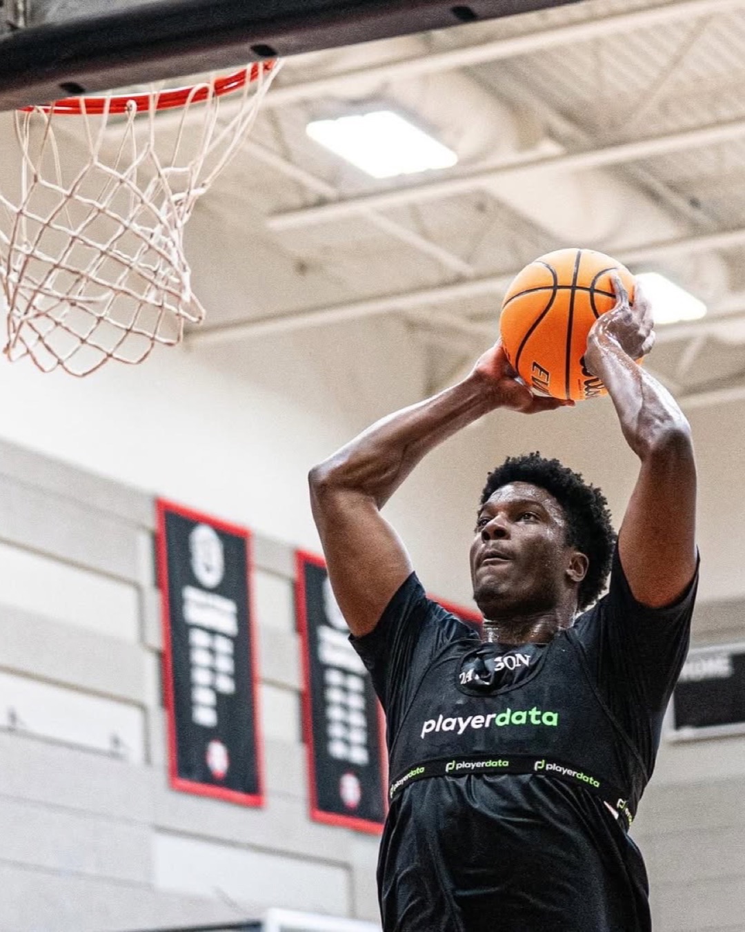 Basketball player in a PlayerData vest rising to the rim during indoor practice