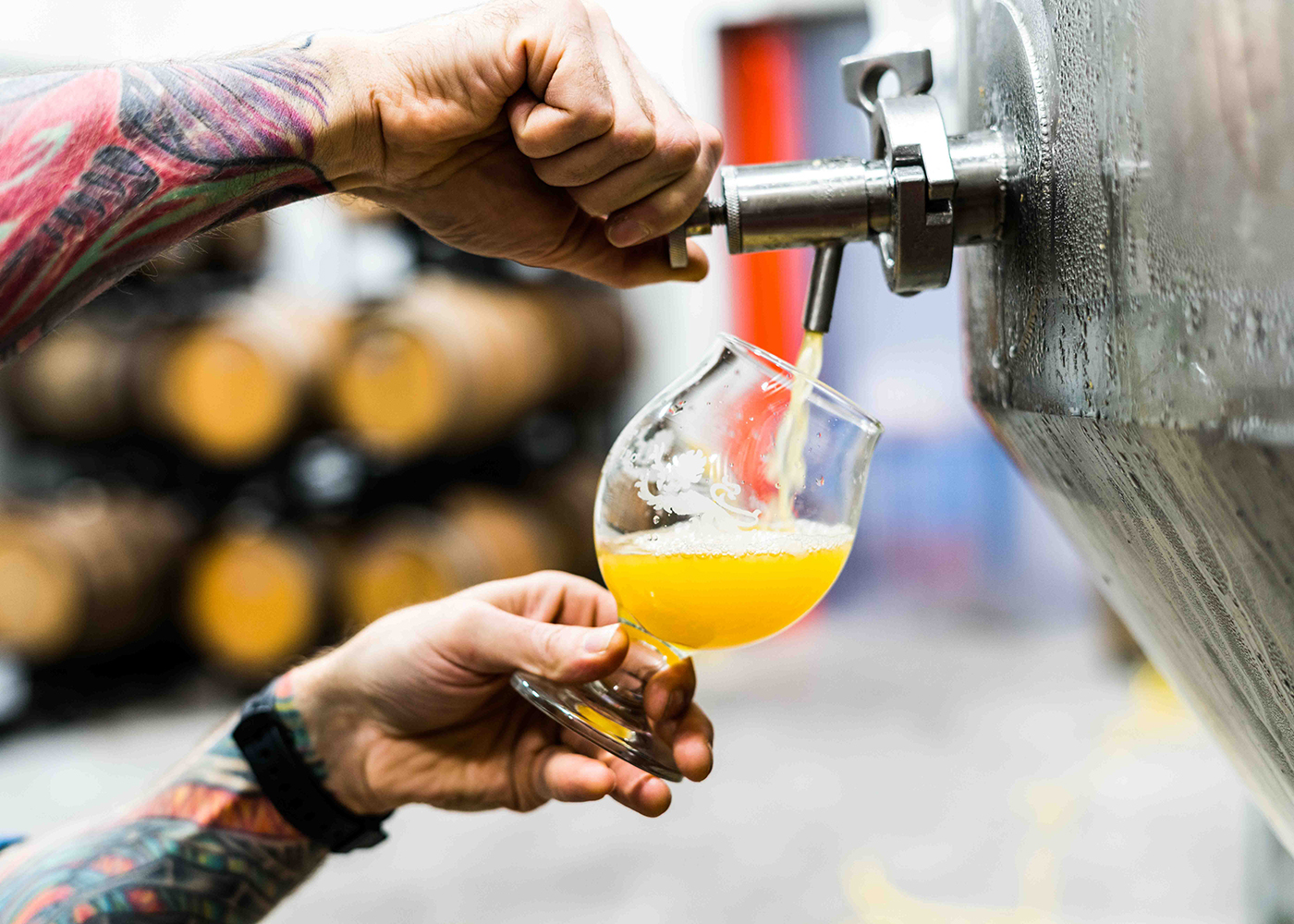 Tattooed man pouring craft beer from vat