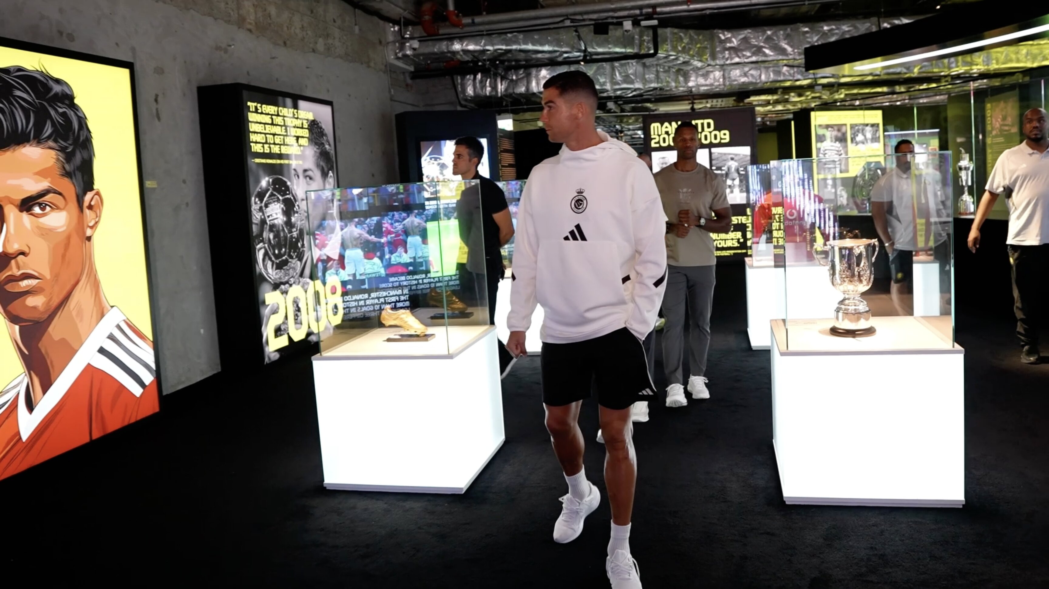 CR7 Life Museum — visitor walking past illuminated trophy cases beside the illustrated Ronaldo portrait wall