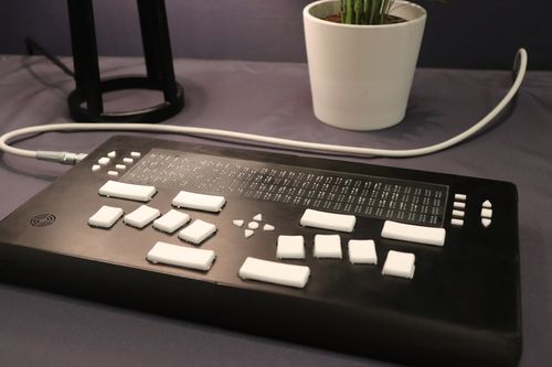 Codex braille display on a desk with hands touching the perkins keyboard