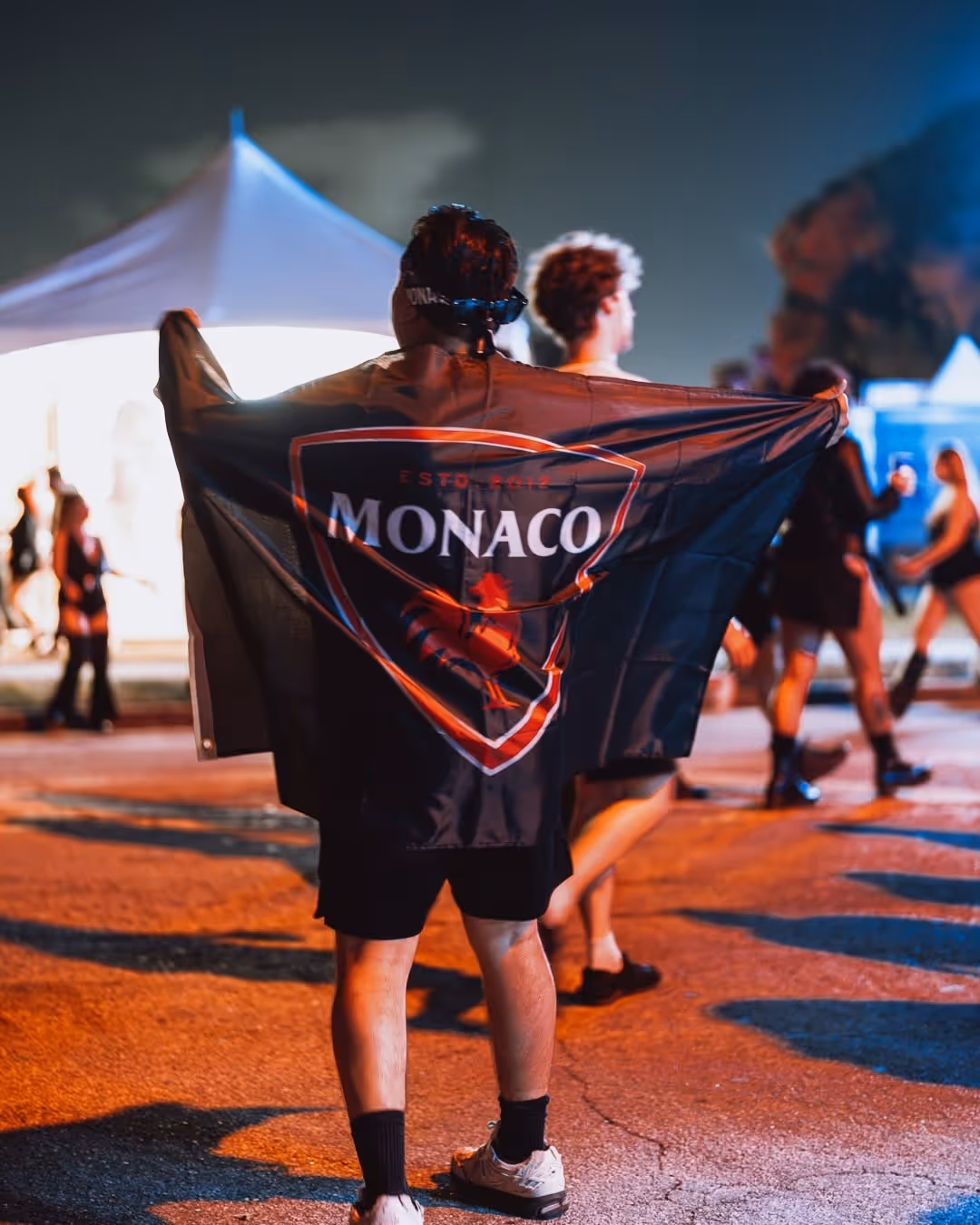 Man draped in a Monaco Cocktails flag while standing outdoors at a night event