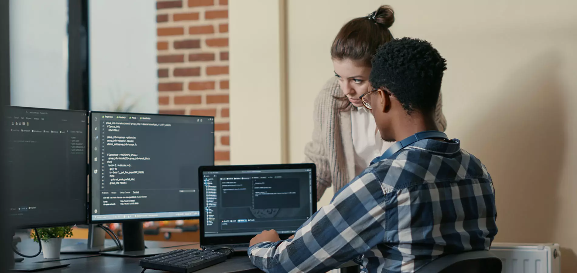 Two programmers discussing with multiple screens