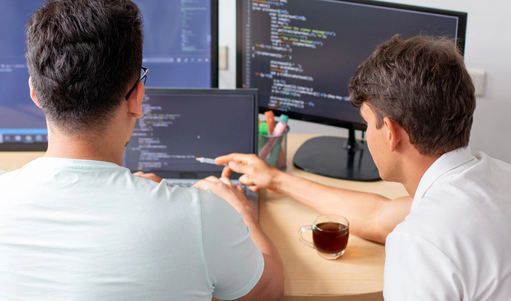 Two programmers working on a desktop computer with three monitors