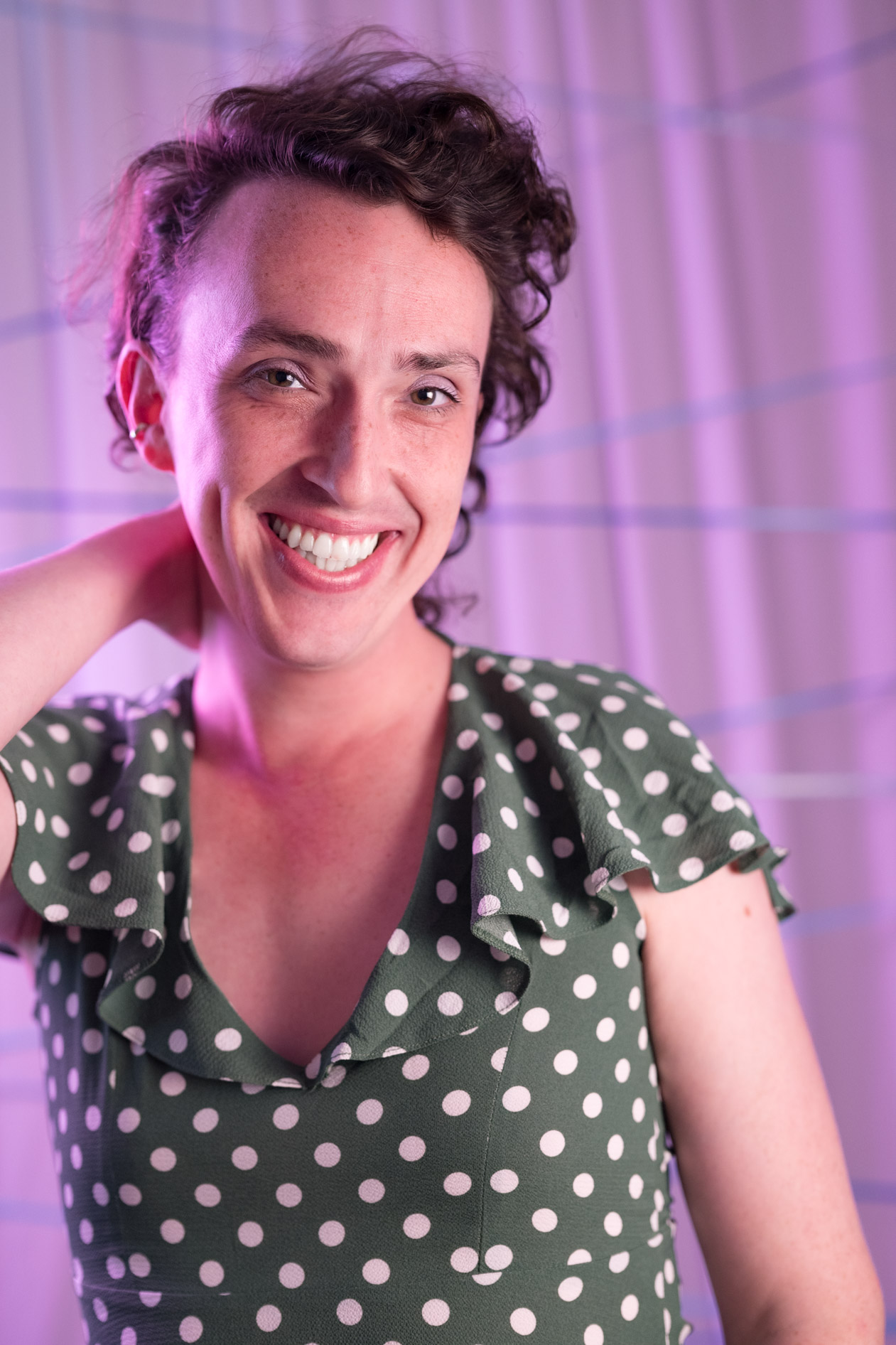 a person smiling widely against a pink backdrop while wearing a green dotted dress