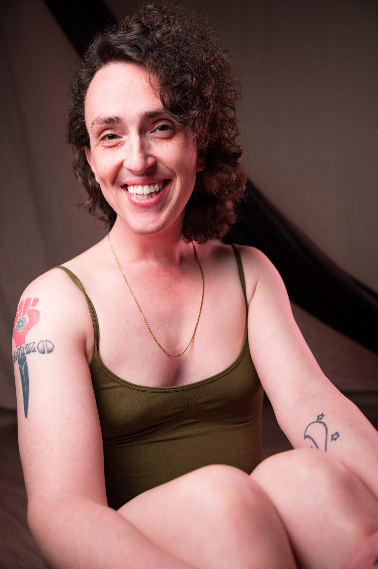 a person with long curly hair smiles widely in a green onesie
