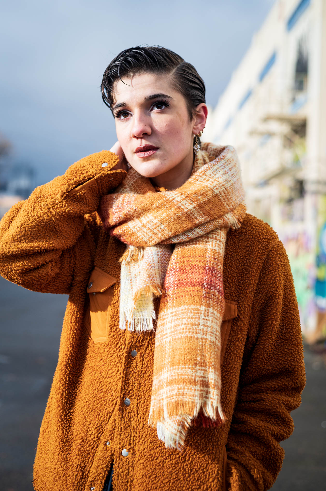 An authentic portrait of a nonbinary person with short hair, wearing a brown fuzzy jacket and a plaid scarf. This image showcases queer-friendly media and inclusive photography in Portland, Oregon.