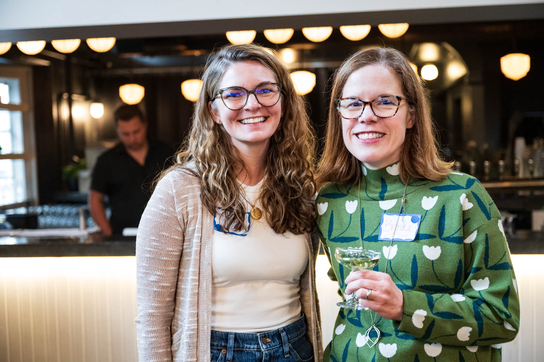 Two smiling colleagues pose for a photo with drinks in their hands at a bar. This is a candid moment captured by a corporate event photographer in Portland, Oregon.