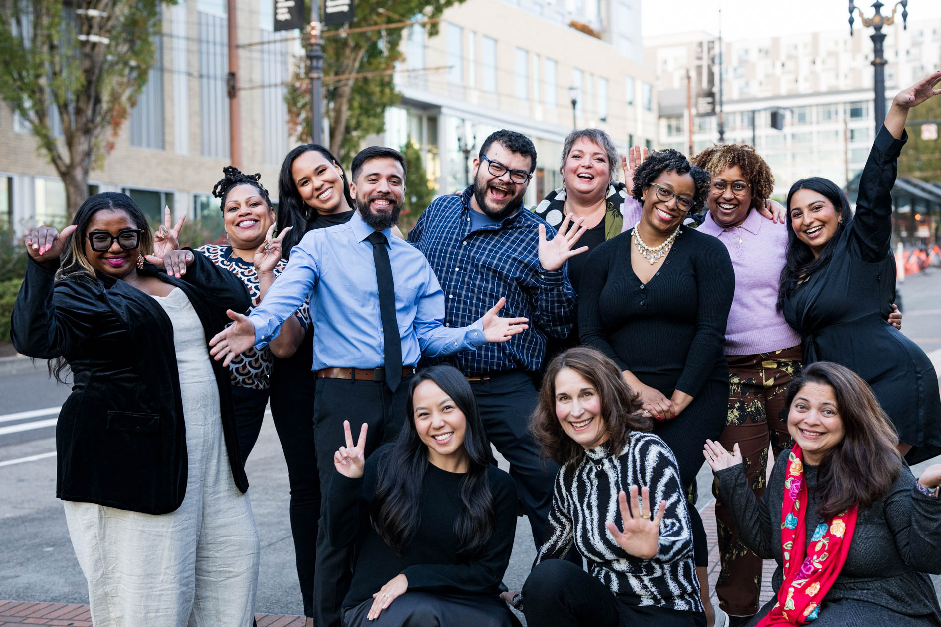 A smiling group portrait of a diverse team outdoors, waving and posing for the camera. This is an example of nonprofit photography by a foundation event photographer in Portland, Oregon.