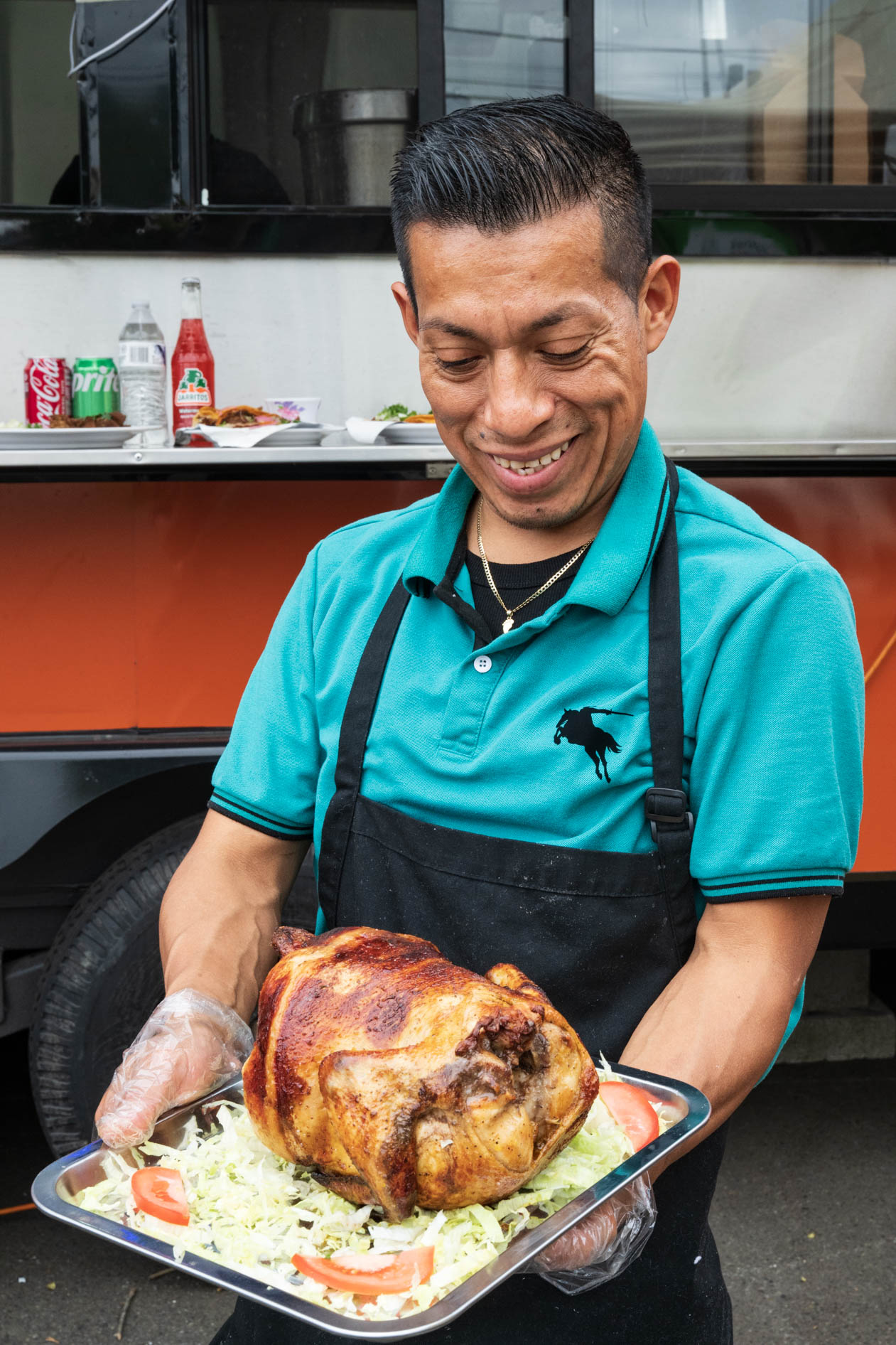 A smiling food business owner holds a platter of a whole roasted chicken. This is an example of on-location commercial photography and brand storytelling in Portland, Oregon.