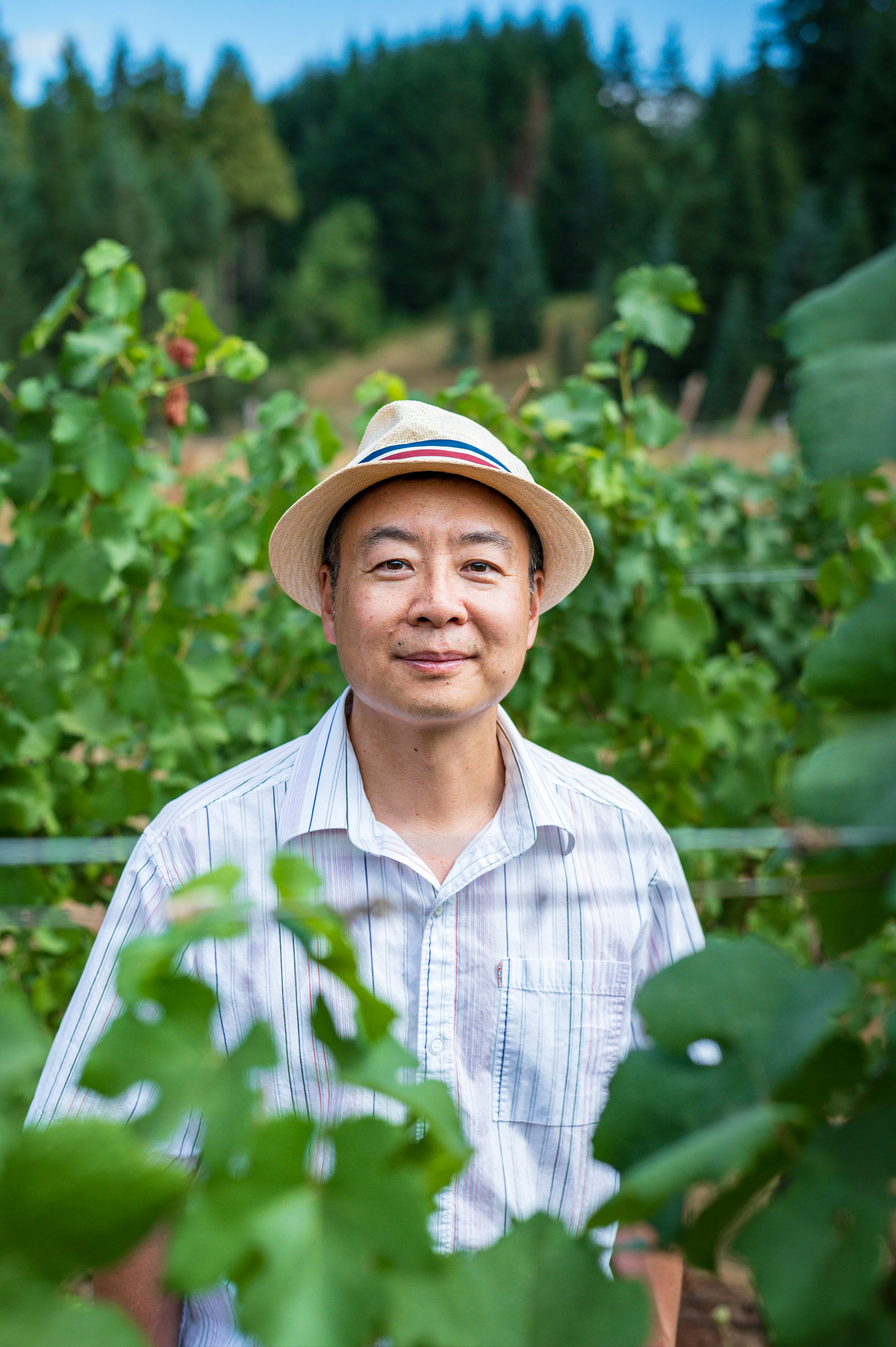 A smiling scientist or business owner wearing a fedora, standing in a vineyard. This is an example of a commercial portrait and brand storytelling photography in Hillsboro, Oregon.