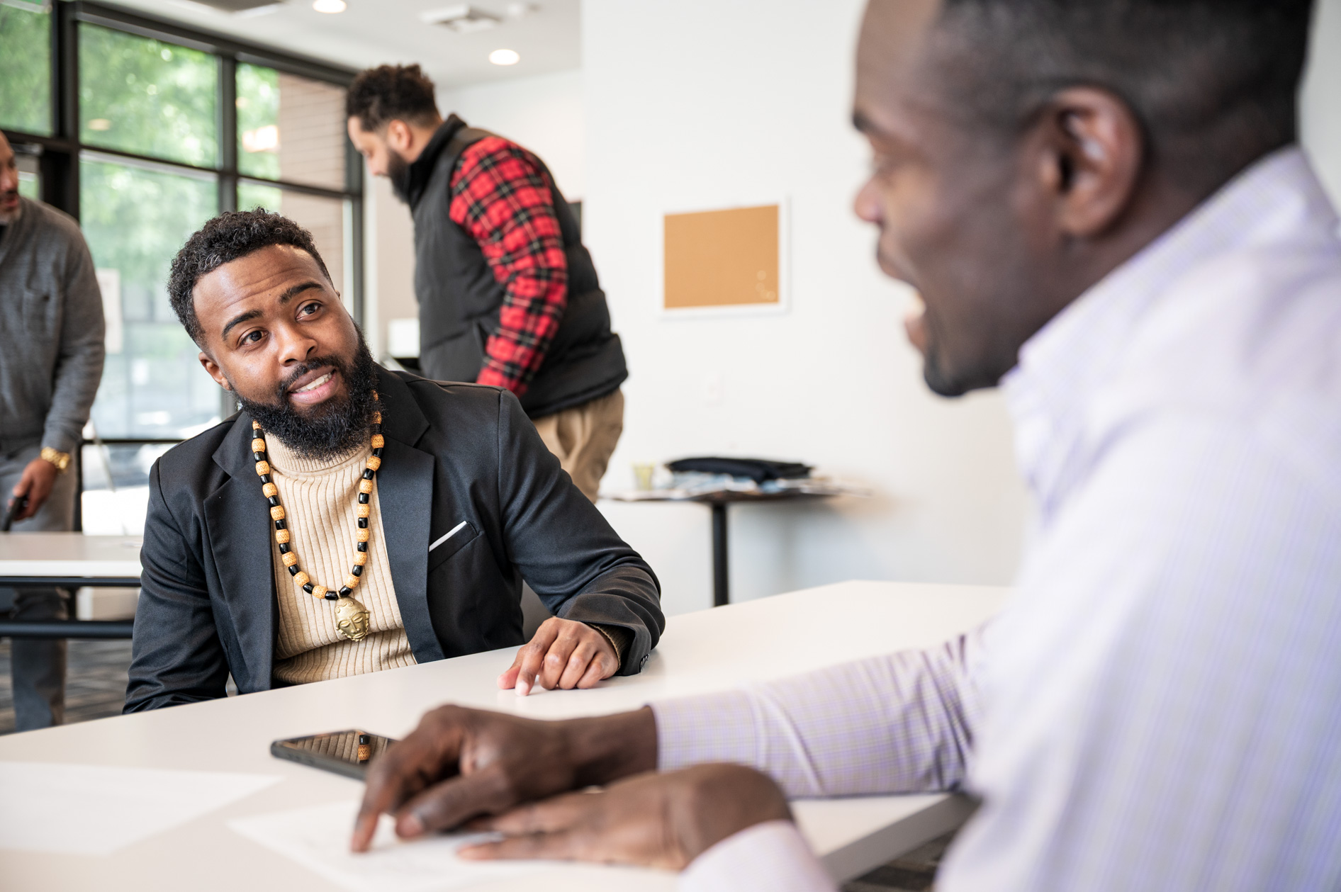 Two men engaged in a lively conversation at a white table in a casual office setting.