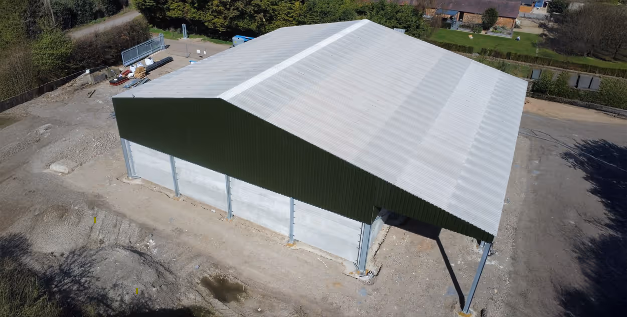 A large, green-roofed warehouse under construction, with visible steel and concrete elements.