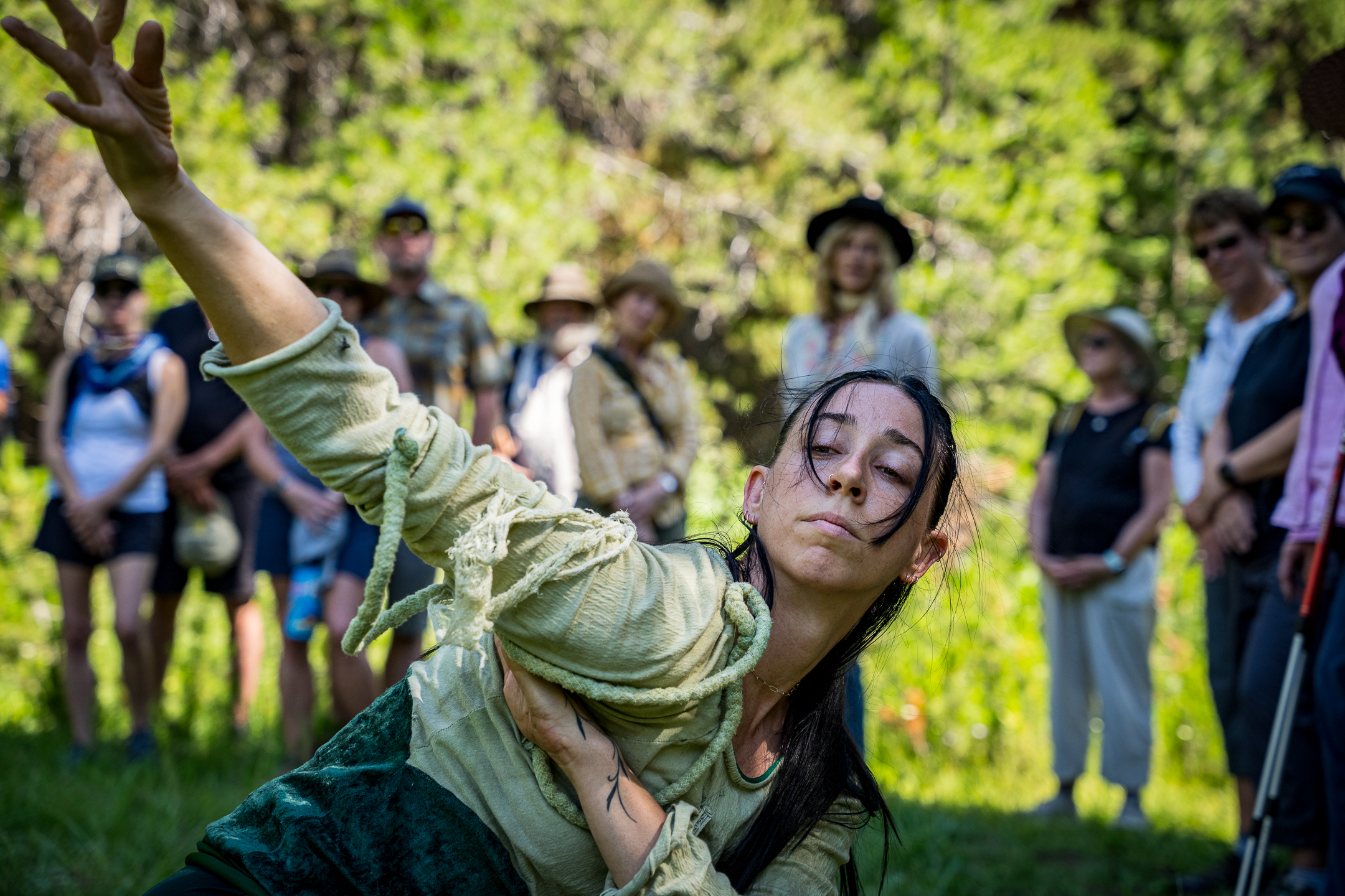 Capacitor dancer performs in front of audience with sunlit forested background