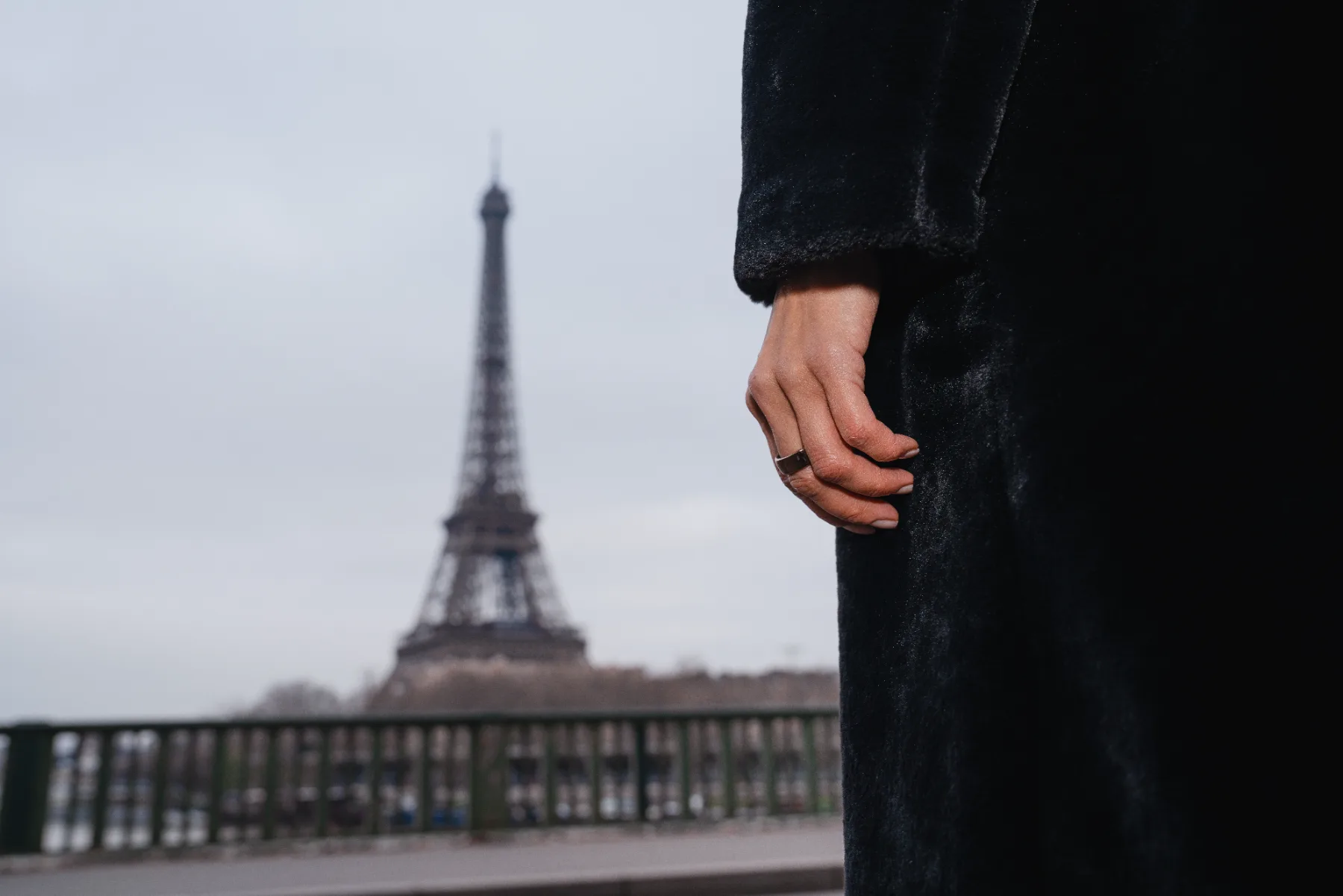 A hand wearing the Circular Ring on a Paris bridge, the Eiffel Tower behind