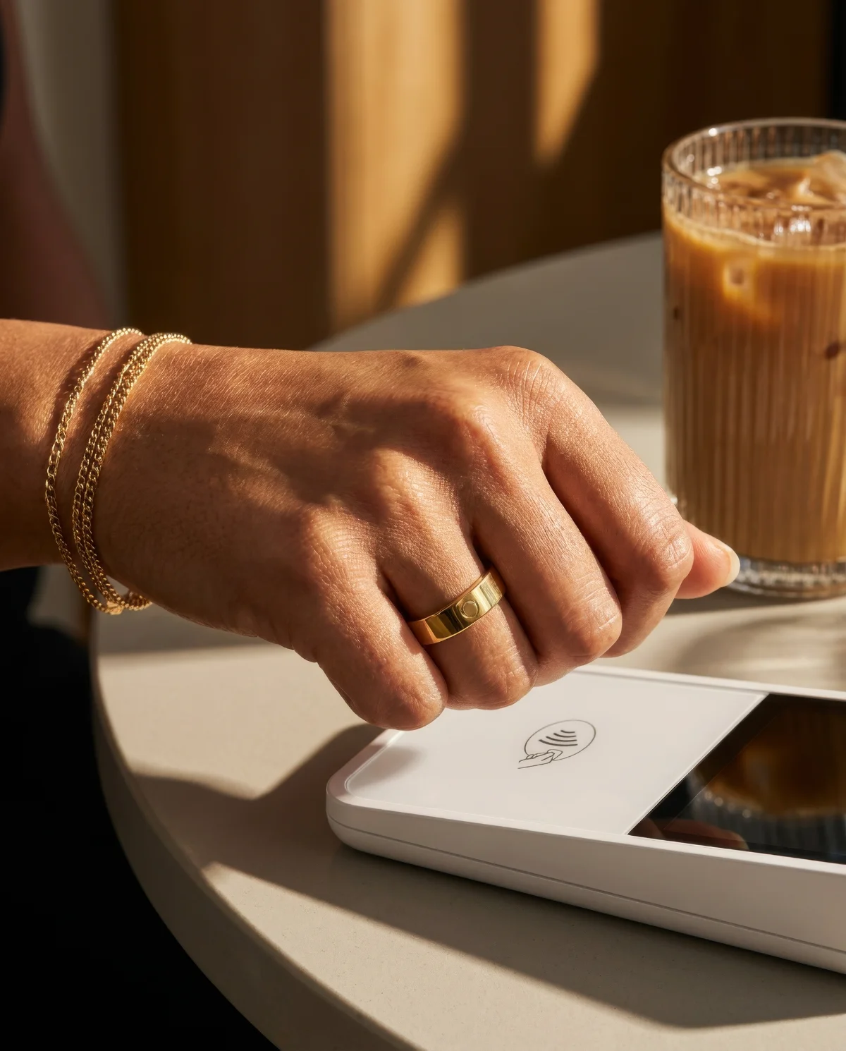 A gold Circular Ring 3 tapping a contactless payment terminal beside an iced coffee