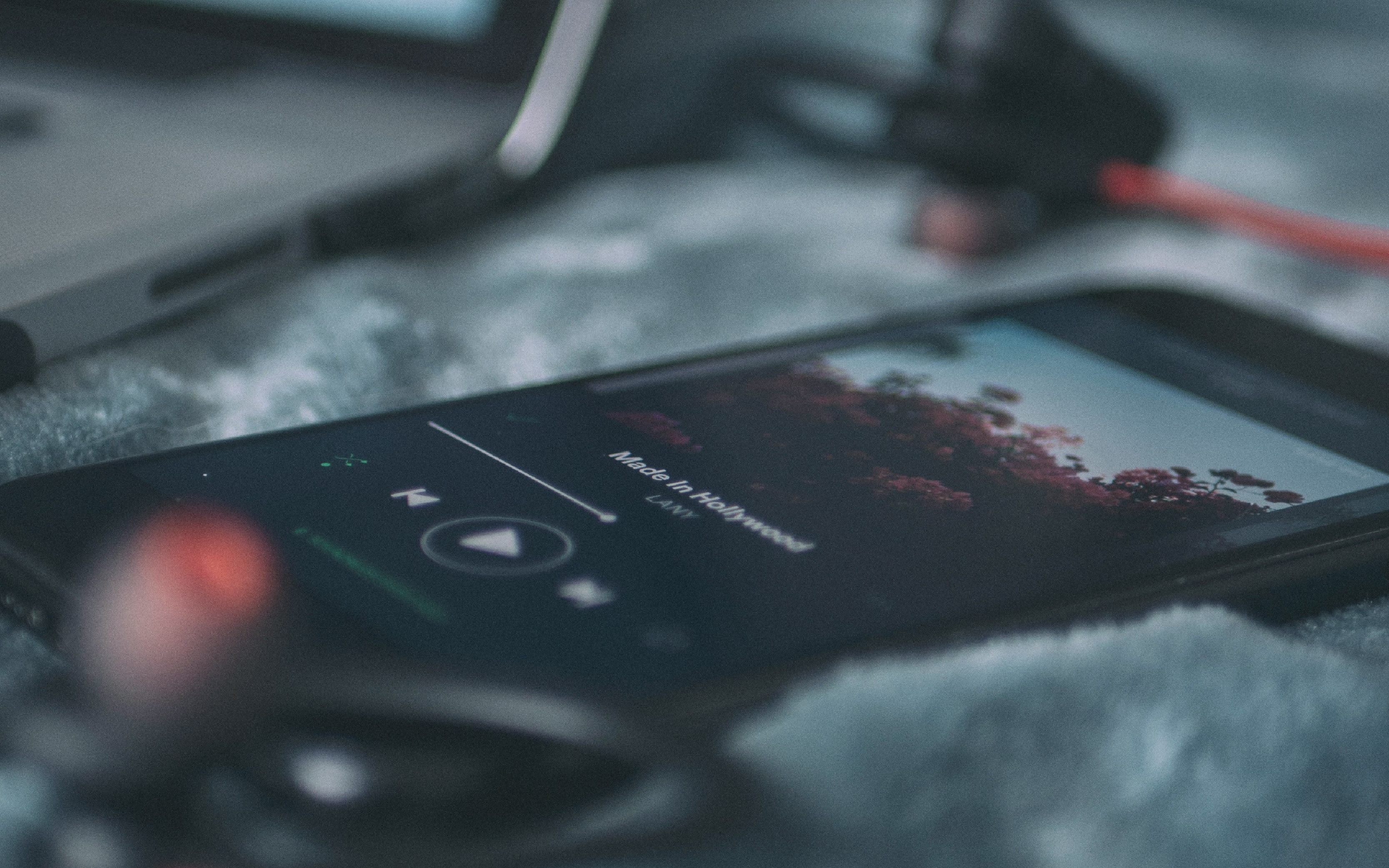 Smartphone lying on a soft surface playing the song 'Made In Hollywood' by LANN, with earphones connected and slightly out of focus.