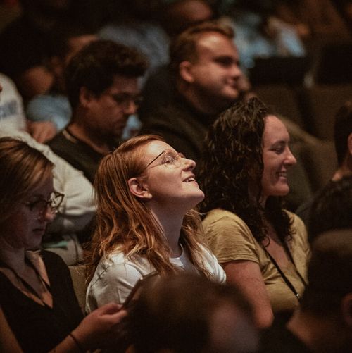 Crowd listening to talks in the theater with a woman in the center smiling and laughing