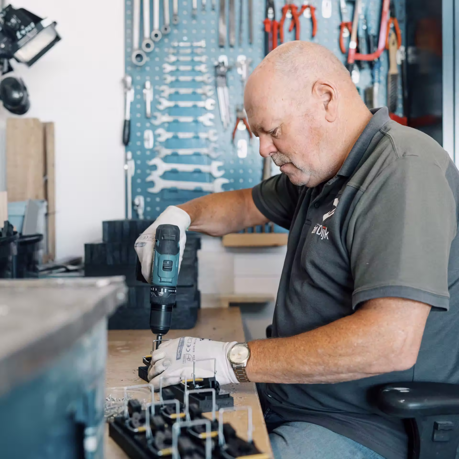 Man die met een elektrische schroevendraaier aan een werkbank werkt in een goed georganiseerde werkplaats.