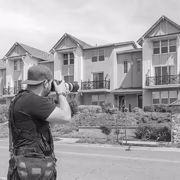 Photographer wearing a cap and gear taking pictures of modern townhouses across the street.