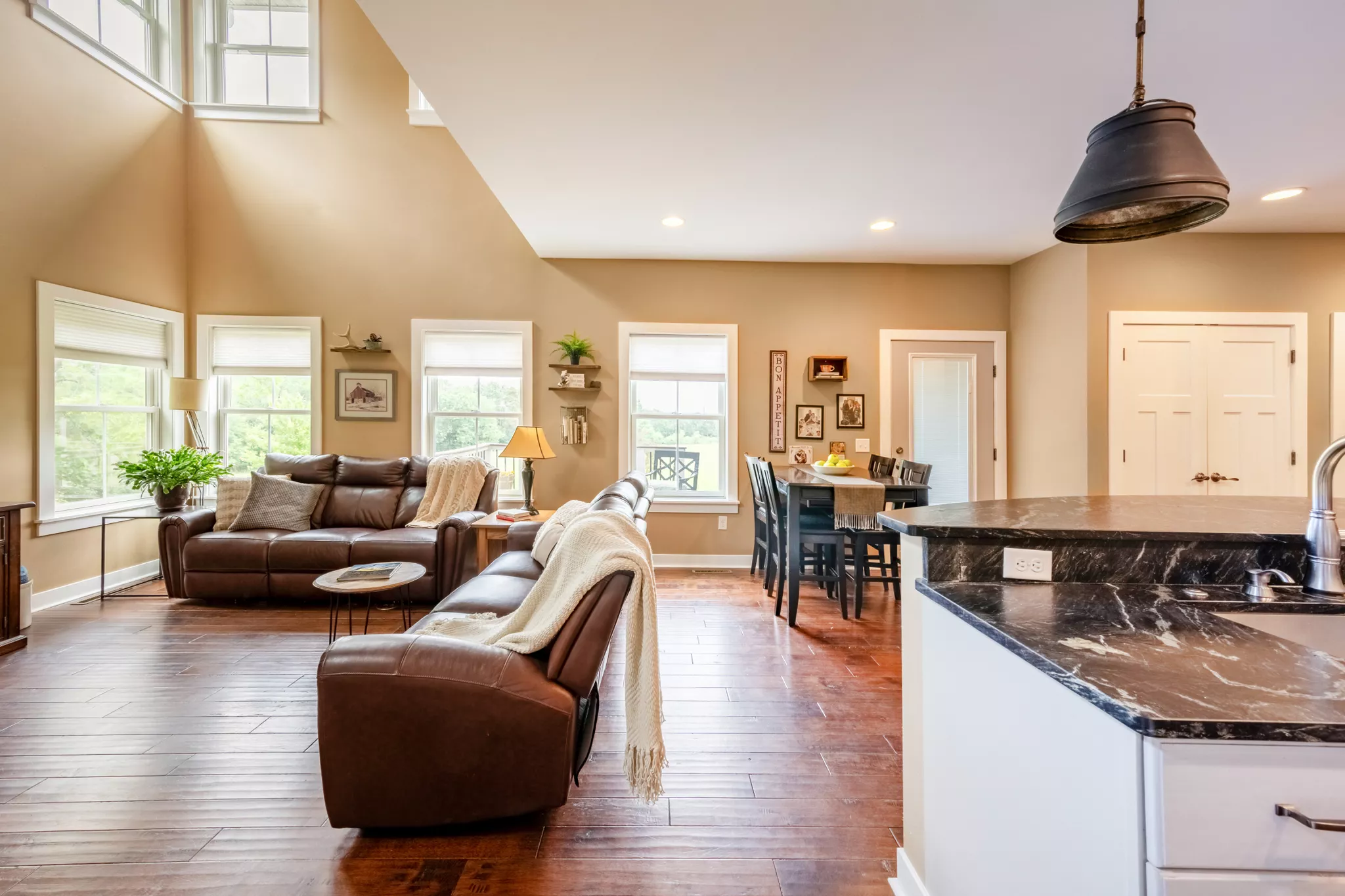 Open living room with brown leather sofas, wood floors, dining table, and kitchen island with sink.