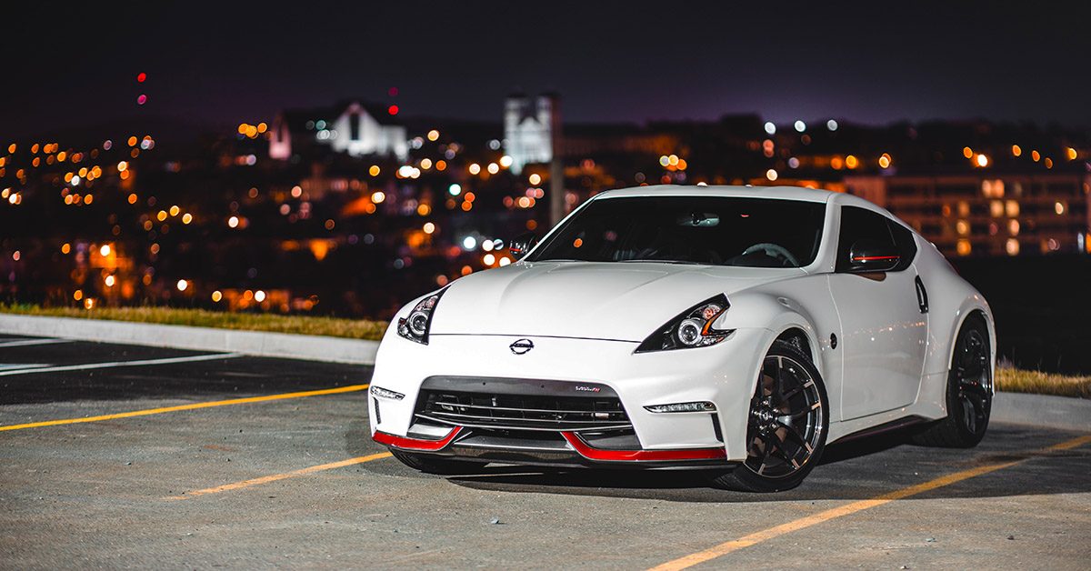 White sports car parked in an empty lot at night with city lights blurred in the background.