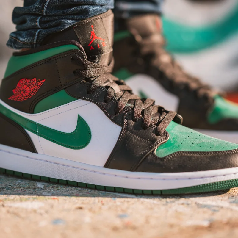 Product photo of a green, white and black high-top sneaker on sand