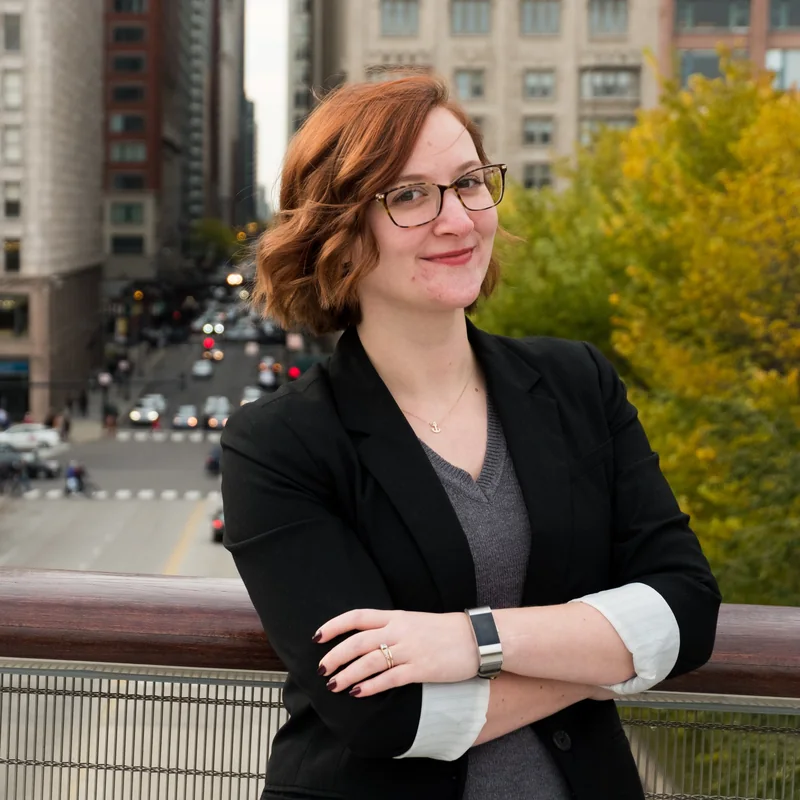 Professional headshot of a woman in a black blazer on a city balcony
