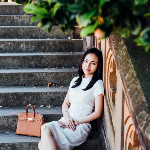 Woman in a white dress seated on outdoor stone steps with a tan handbag