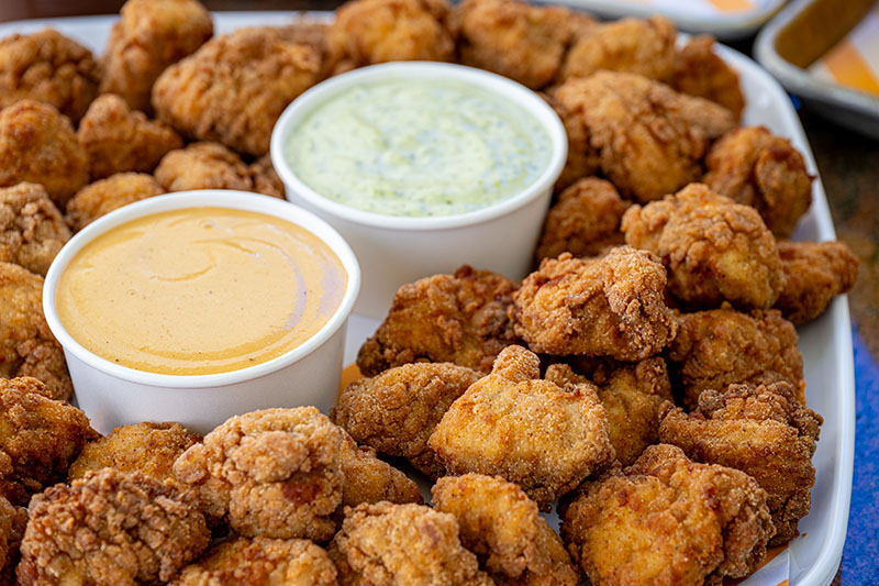 Tray of golden brown fried chicken bites accompanied by two dipping sauces, one creamy yellow and one green herb sauce.